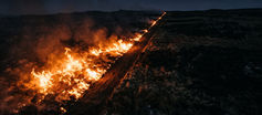 A controlled fire burns along one side of a dark hillside at night, while a clear firebreak prevents the flames from crossing into untouched ground.