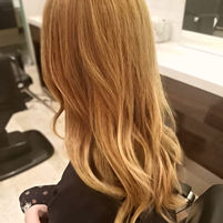 Profile view of a client with long, straight warm honey blonde hair color.