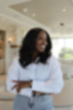 Smiling woman in a white button-down shirt standing in a modern, light-filled living room.