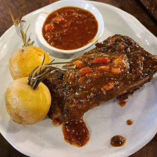 white plate with 2 potatoes skewered with rosemary, small rack of ribs topped with bbq sauce, and a side dish of additional bbq sauce