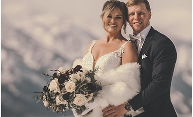 a portrait of a bride and groom holding her winter bridal bouquet with snowy mountains in the background
