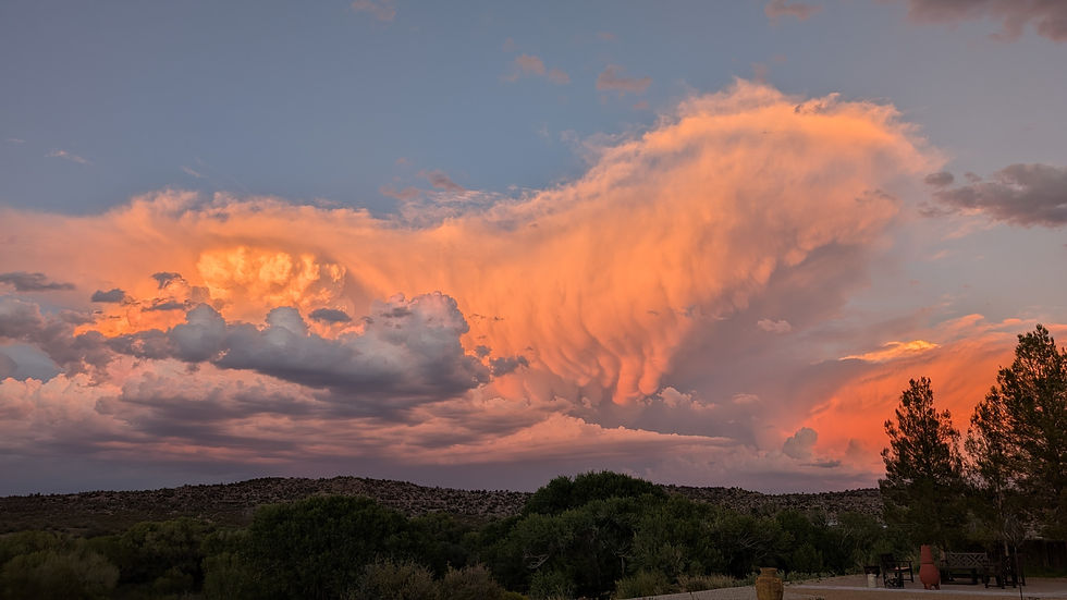 Vibrant orange clouds at sunset over a hilly landscape. Trees in the foreground create a serene and dramatic scene against the evening sky.