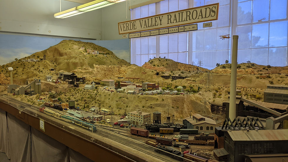 Model railroad diorama, with a smelter in the near corner and towns climbing the hills beyond.