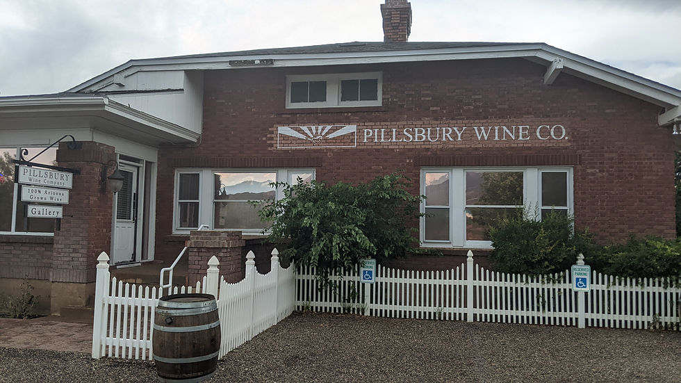 Closeup of the Pillsbury Wine Co, located in an old, red-brick building with while window and roof trim, and a white picket fence.