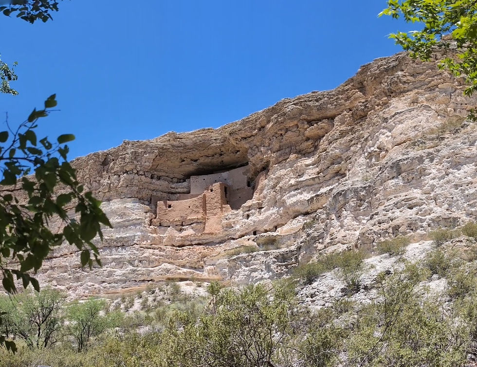Ancient cliff dwelling embedded in rocky canyon under clear blue sky, with green foliage at the bottom creating a tranquil scene.