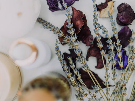 Flat lay of dried lavender sprigs with purple petals and softly blurred skincare bottles, evoking a calm, mindful pre-holiday skincare ritual.