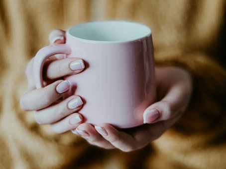 Hands holding a warm pink mug against a cozy sweater, symbolizing comfort, softness, and gentle winter self-care rituals
