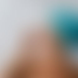 A woman with a light turquoise towel wrapped around her hair, smiling as she applies cream to her nose, symbolizing fresh skincare rituals for 2025