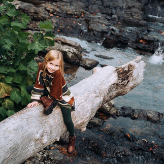 tween girl sitting on a log over a creek