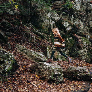 tween girl in stylish fall sweater jumping rock to rock