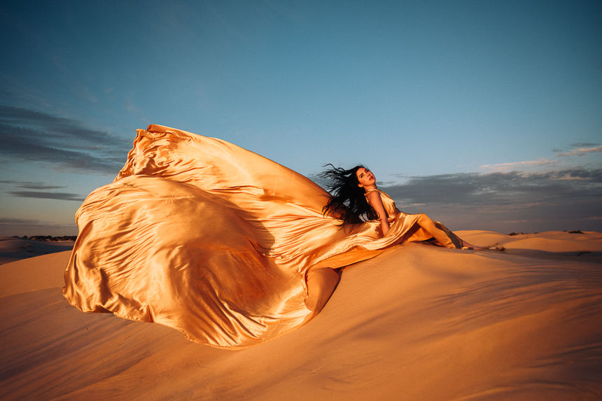 Girl in fold flying dress on sand dunes