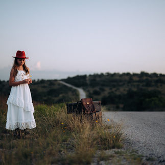 tween girl in field with yellow flowers white dress and red hat