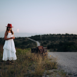 tween girl in field with yellow flowers white dress and red hat