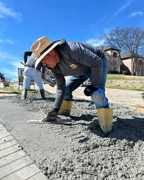 The Pro Quality team uses a concrete float to smooth and level freshly poured concrete, creating a polished surface for a newly installed concrete walkway in Lewisville, TX.