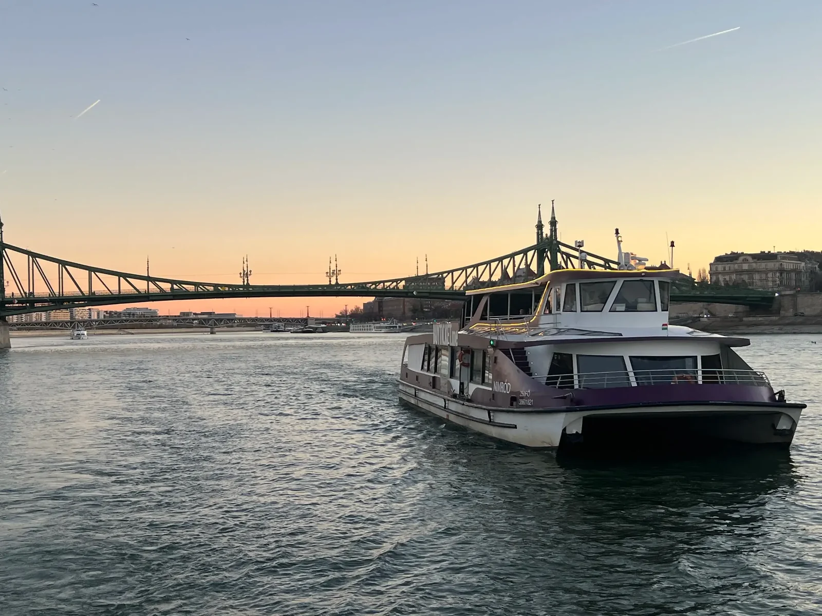 Private boat cruise Budapest at sunset, a boat sailing on the Danube with Liberty Bridge in the background.