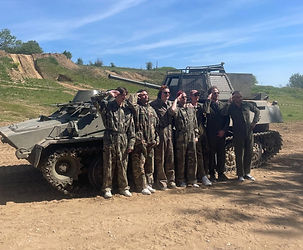Tank driving Budapest group photo, friends in camouflage suits posing and saluting beside a tank on an off road track.