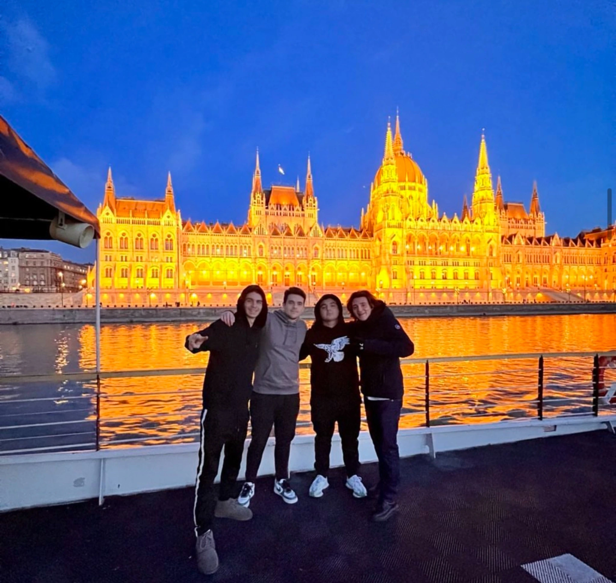 rivate boat cruise Budapest at night, friends posing on deck with the Hungarian Parliament Building illuminated across the Danube.