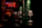 The stylish, dimly lit interior of Mitico in Budapest, featuring elegant crystal lamps on dark marble tables, with moody green and red lighting that creates a sophisticated ambiance. This chic cocktail bar is perfect for stag groups seeking a refined and atmospheric venue to enjoy expertly crafted drinks.