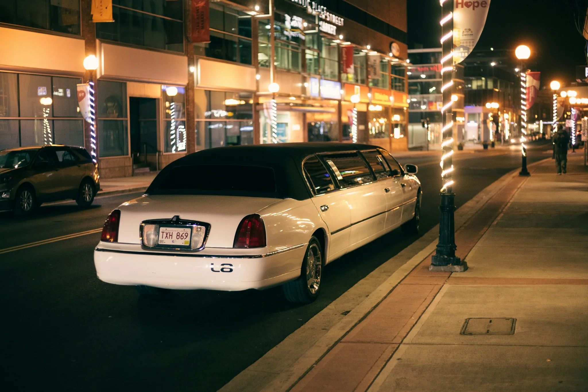 White stretch limousine parked at the curb on a well lit city street at night with shopfronts and streetlights in the background, Budapest Strip Limo pickup.