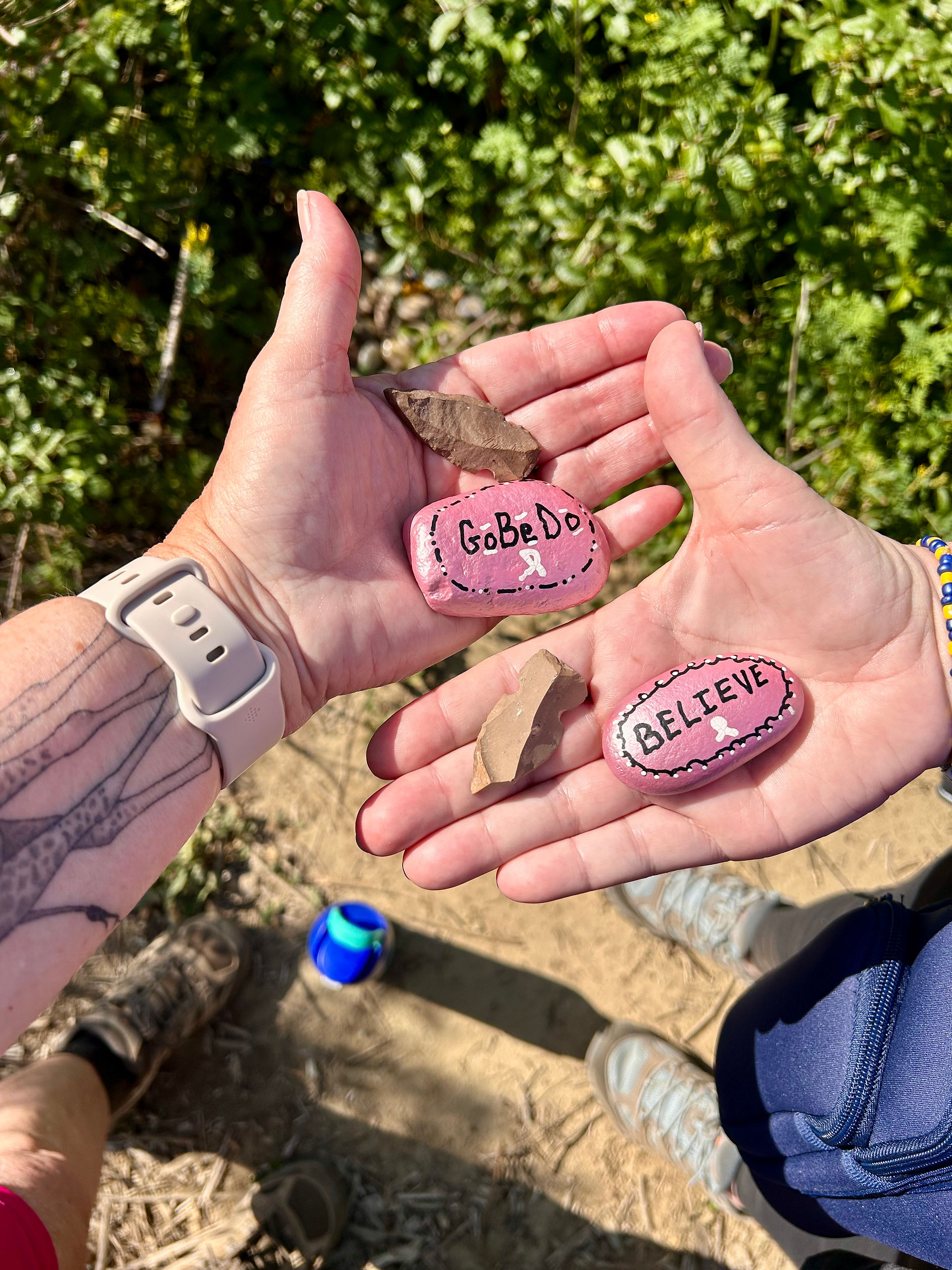 Two women's hands holding arrowheads and bright pink rocks.