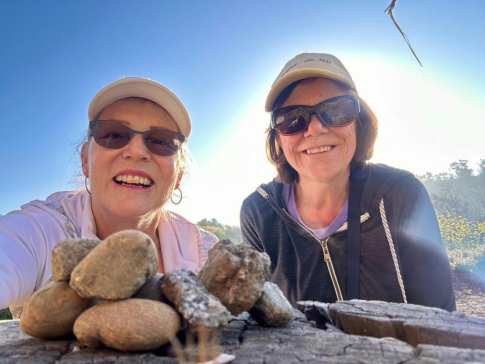 Two women outside posing in front of a small rock formation.