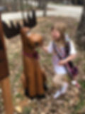 A young girl pets a wooden carving of a moose.