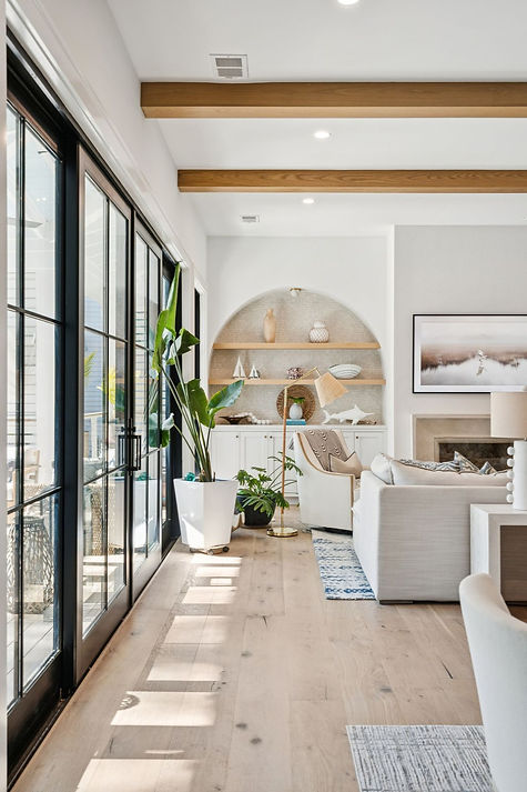 Modern living room with built in shelfs, light wood floors, beige sofas and a house plant.