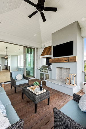 Inviting screen porch with a cozy outdoor fireplace and grill, part of a Cape Cod style oceanfront home.