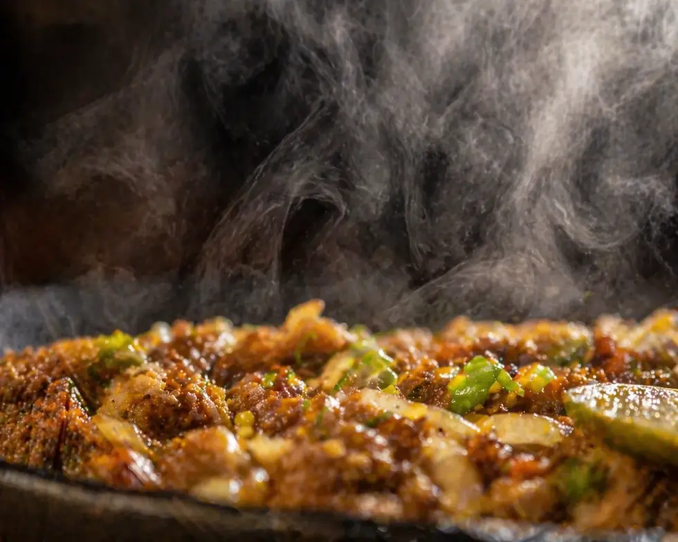 Steaming hot dish with sizzling meat and vegetables, topped with green herbs and a lime wedge, creating a savory and appetizing mood.