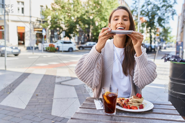 Water-marked stock photo of a woman in a shrug cardigan photographing her pancake brunch and iced tea while sitting outside.