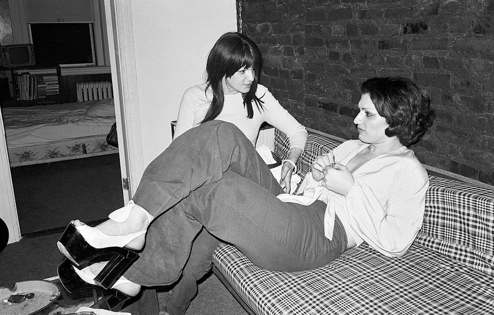 Female impersonator and friend hashing out problems seated on couch.
