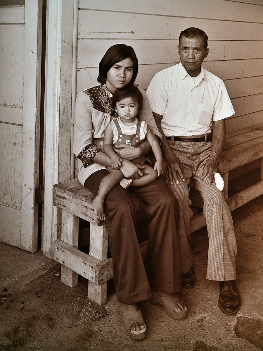 Three Generations seated, Father with finger bandage, daughter holding her daughter at labor camp.