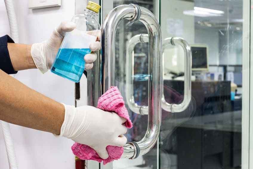 Cleaning worker wiping down door handles at an office