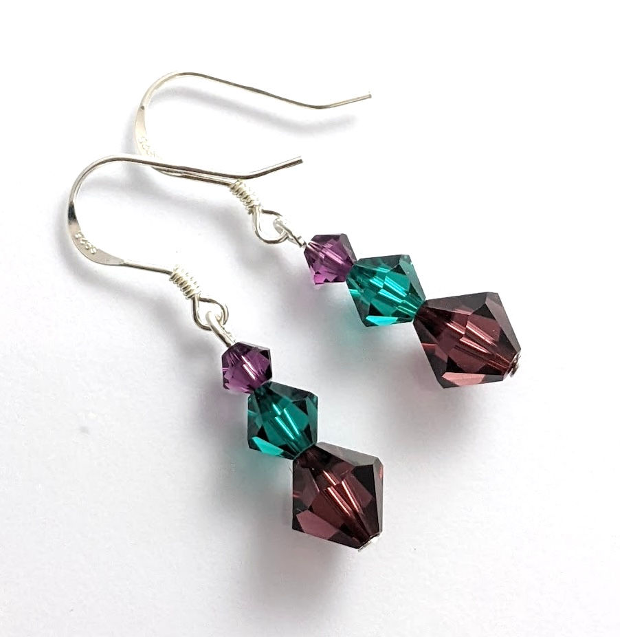 A pair of handcrafted earrings with three graduated burgundy and emerald Austrian crystals on sterling silver hooks.