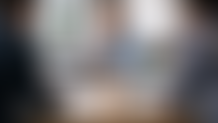 Drei Personen sitzen in einer modernen Besprechung an einem Konferenztisch. In der Mitte prüft ein Kunde nachdenklich zwei Website-Angebote, links präsentiert ein professionell gekleideter Anbieter eine hochwertige, strukturierte Lösung, rechts zeigt ein lässigerer Anbieter eine einfachere und unordentlichere Website-Präsentation.