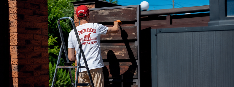Penrod Lumber & Fence crew member painting a wood fence on a ladder in Ocala, Florida
