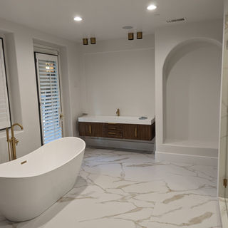 "Modern luxury master bathroom remodel in Palm Springs, CA featuring custom floating his and hers vanities with white quartz countertops, brushed gold faucets and hardware, and a freestanding soaking tub with floor-mounted brushed gold filler across from a walk-in shower. Large-format porcelain Calacatta gold tiles with subtle gold movement complete this high-end design. Ideal for homeowners in Palm Springs, Palm Desert, Rancho Mirage, Indian Wells, La Quinta, and Cathedral City seeking a premier bathroom remodeling contractor