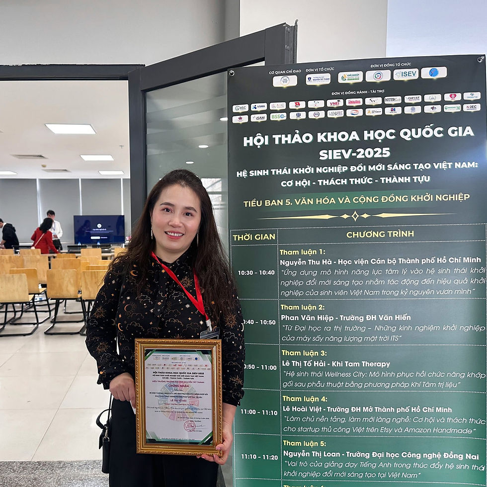 Master Sridevi Tố Hải stands smiling with a framed certificate in hand at the National Scientific Conference SIEV-2025 in Vietnam. Behind her is a conference schedule poster featuring her presentation on Khi Tam Therapy.