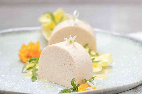 Hausgemachte Pastete in Scheibenauf einem hellen Teller, dekoriert mit essbaren Blüten, frischen Kräutern und Blütenblättern. Die minimalistisch Foodfotografie vermittelt Eleganz und Fine-Dining-Qualität. 