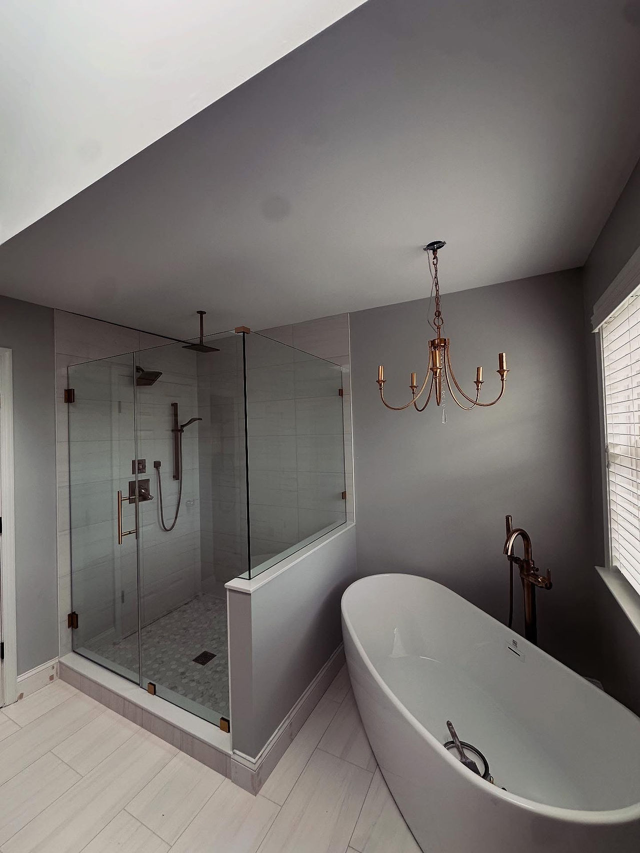 Wide view of the finished bathroom with frameless shower and freestanding tub.