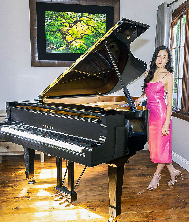 Miist standing next to a classic black piano in an artistic sunlit room.