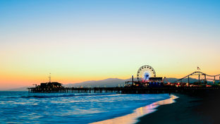 Beautiful sunset photo of the Santa Monica Pier all the way across the Pacific Ocean as the sun sets behind the LA mountains in the cover of LA Today's January Events Guides