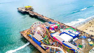 A beautiful day in June overlooking the Santa Monica Pier and Santa Monica Beach in LA County. A crowded scene full of energy and relaxing blue-teal water by the warm sandy beach.