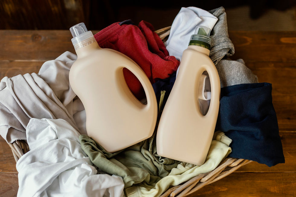 Laundry basket with assorted folded clothes and two beige detergent bottles on a wooden table.