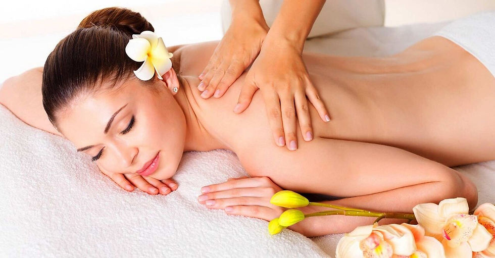 Woman receiving a back massage, lying on a white towel. Her hair is adorned with a flower. Yellow and peach flowers in the foreground. Calm ambiance.