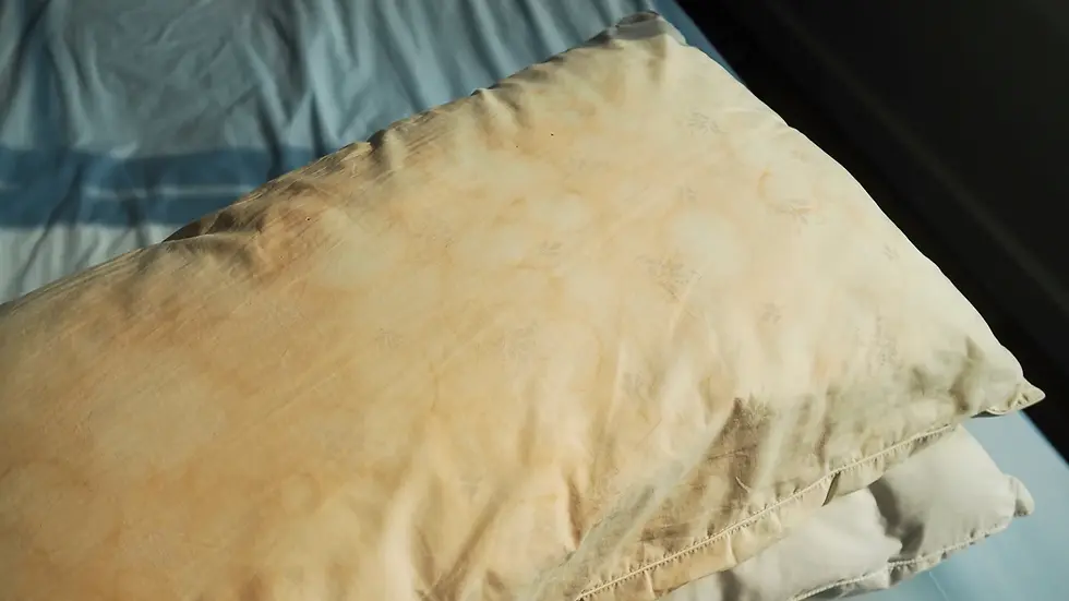 A yellowing pillow with faint floral patterns rests on a bed with blue sheets, creating a worn and nostalgic atmosphere.