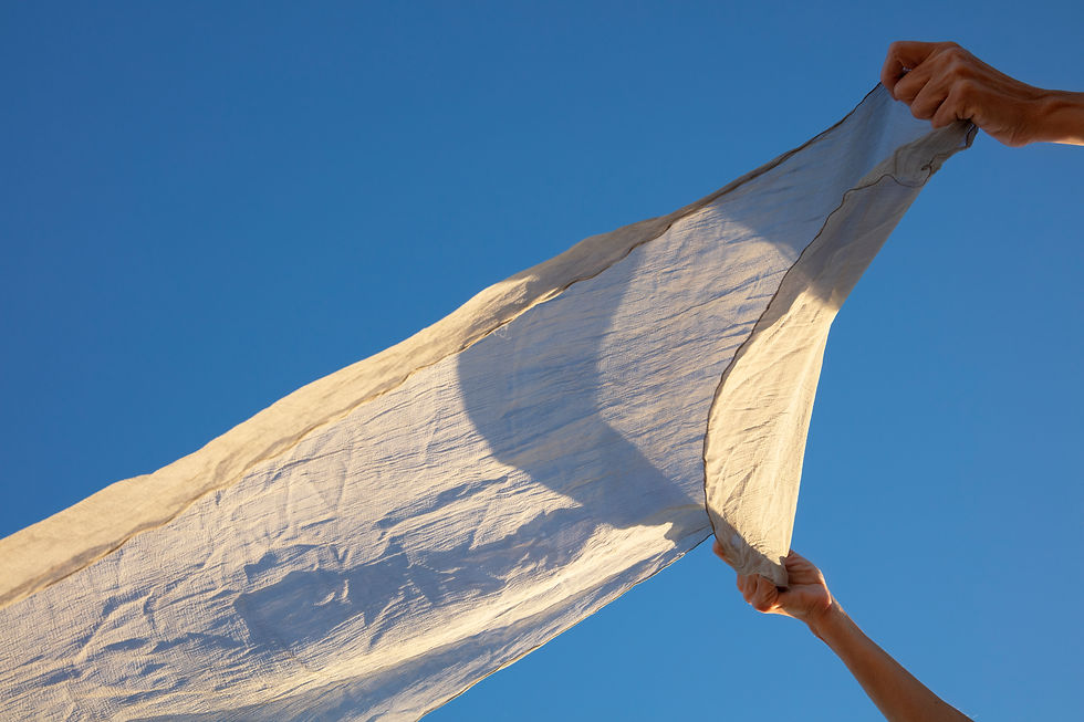 Two hands stretch a white cloth against a clear blue sky, creating a bright, airy scene
