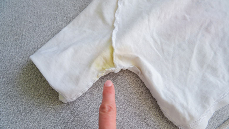 Finger pointing at a white garment with yellow stain on a gray surface, emphasizing a laundry issue or stain awareness.