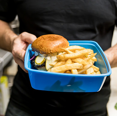 Man holding out a burger and fries in a square, blue Friendlier reusable container