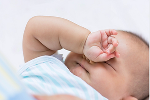 Baby rubbing their eyes and covering their face, showing signs of tiredness